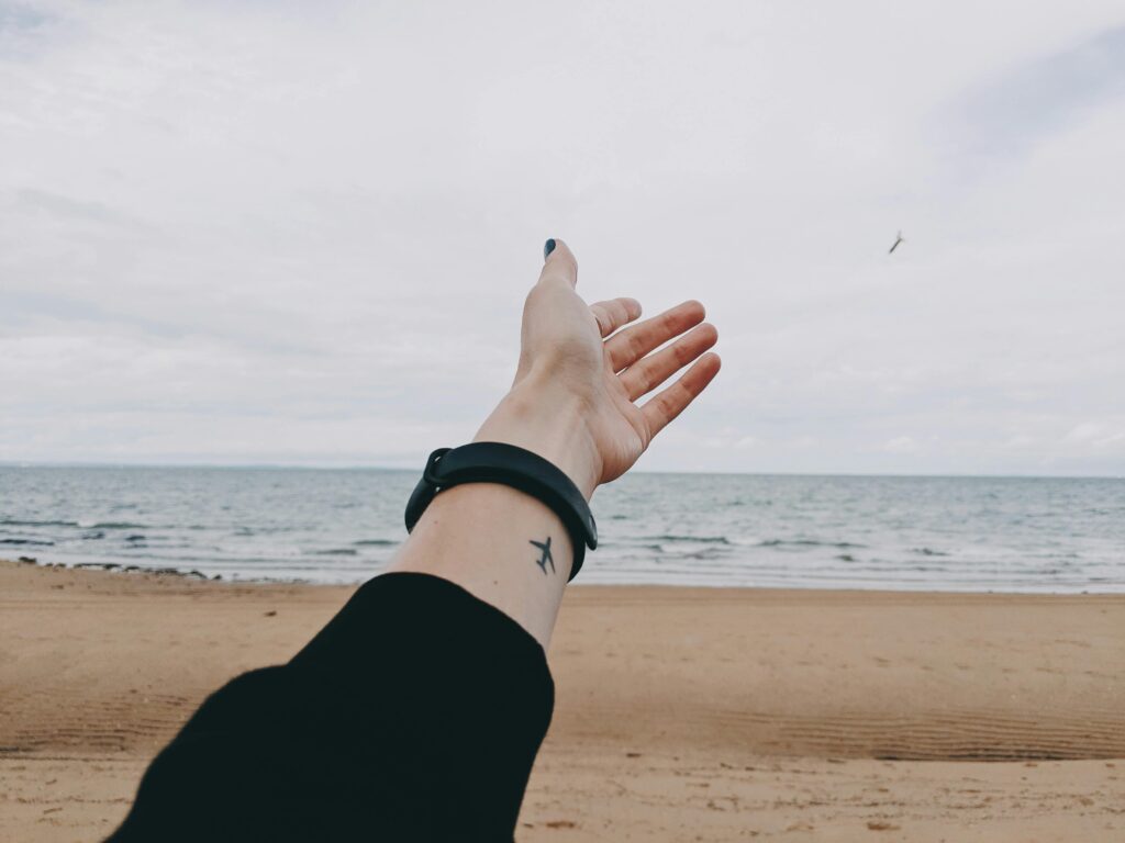 Tattooed hand reaching out towards the ocean on an Australian beach, symbolizing freedom.