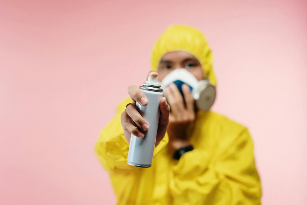 Individual in yellow hazmat suit sprays disinfectant, focusing on hygiene and safety.