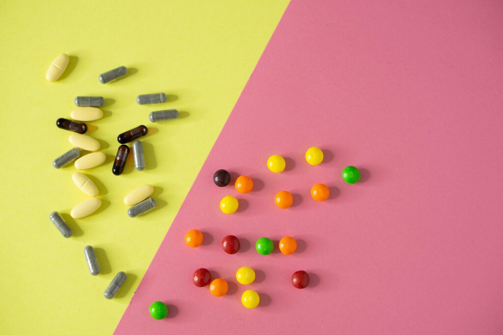 A flat lay of assorted pills and candies on a vibrant yellow and pink background, highlighting the contrast between medication and sweets.